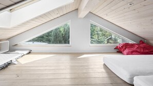 Una habitación con techo inclinado, dos ventanas grandes, una cama y una manta roja.
