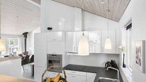 Una cocina moderna con armarios blancos, una isla central, luces colgantes y una cesta de verduras.