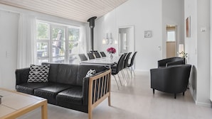 Una sala de estar moderna con un sofá de cuero negro, una mesa de centro de madera y un comedor con una mesa de vidrio y sillas negras.