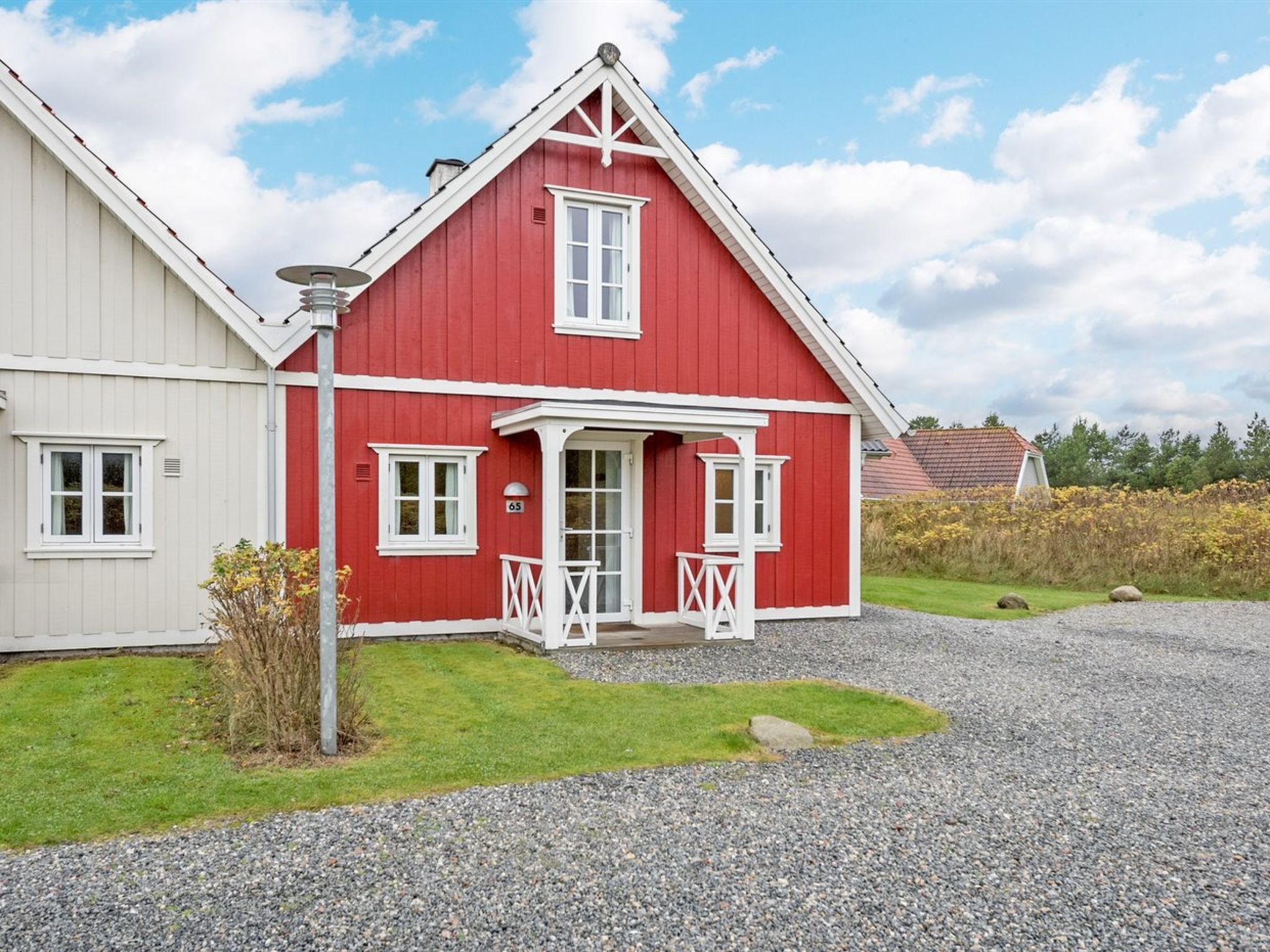 Een rode woning met een witte veranda en een grindpad.