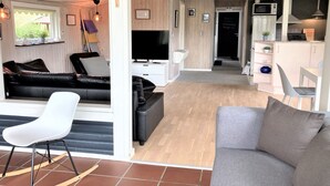 Ein modernes Wohnzimmer mit einer schwarzen Ledersofa, einem weißen Sessel und einem Fernseher.