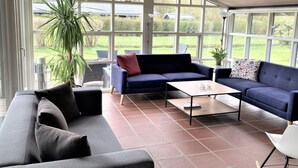 Ein geräumiger Wohnbereich mit großem Fenster, einem blauen Sofa, einem Couchtisch und einem Blumentopf.