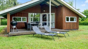 Eine Holzhütte mit einer überdachten Terrasse, einem Grill und Liegestühlen.