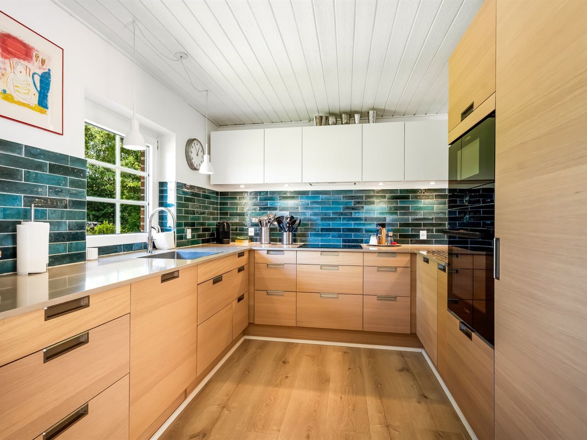 Une cuisine moderne avec des meubles en bois, une cuisinière noire et une fenêtre donnant sur un paysage verdoyant.