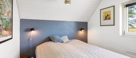 A bedroom with a bed, two wall-mounted lamps, a small stool, and a window with a view.