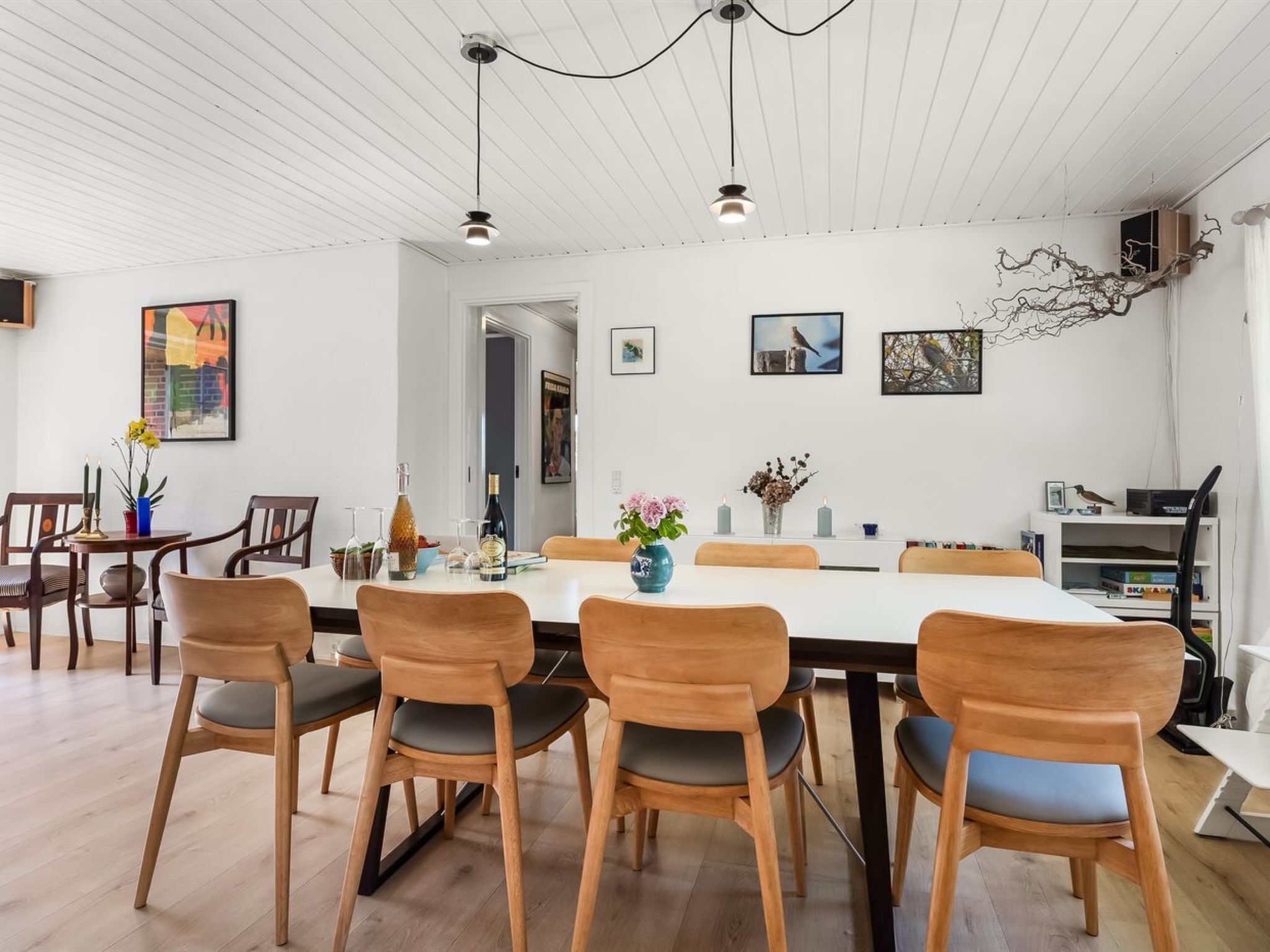 Un comedor con una mesa blanca, sillas de madera y un diseño moderno en el techo.