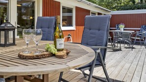 Une terrasse extérieure avec une table ronde en bois, deux chaises, une bouteille de vin et une lanterne.