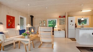 Un intérieur moderne avec un plafond en bois, un canapé, une table à manger, une chaise, un coin cuisine et une cheminée.