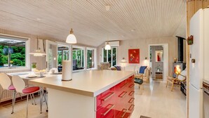 Une cuisine spacieuse dotée d’un grand îlot central, de luminaires suspendus modernes et offrant une vue sur un paysage verdoyant.