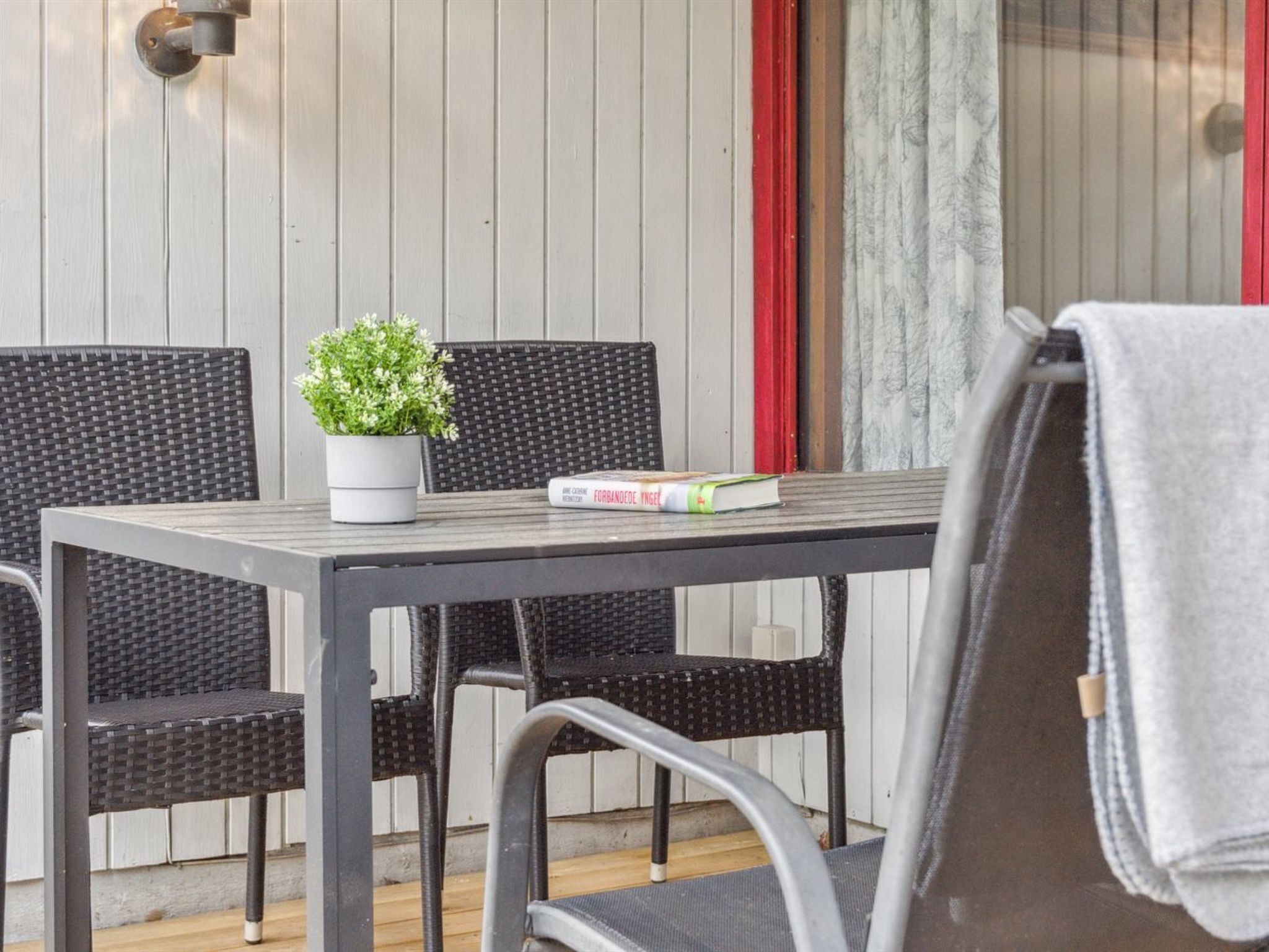 A patio area with a table, two chairs, a potted plant, and a book.