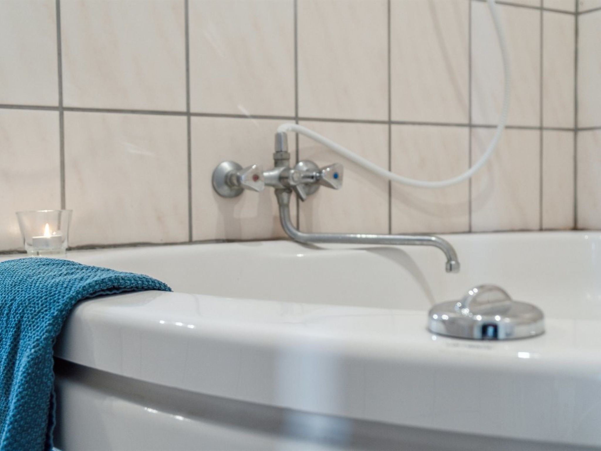 Une salle de bain avec une baignoire, une douchette à main et une bougie en verre posée sur le sol.