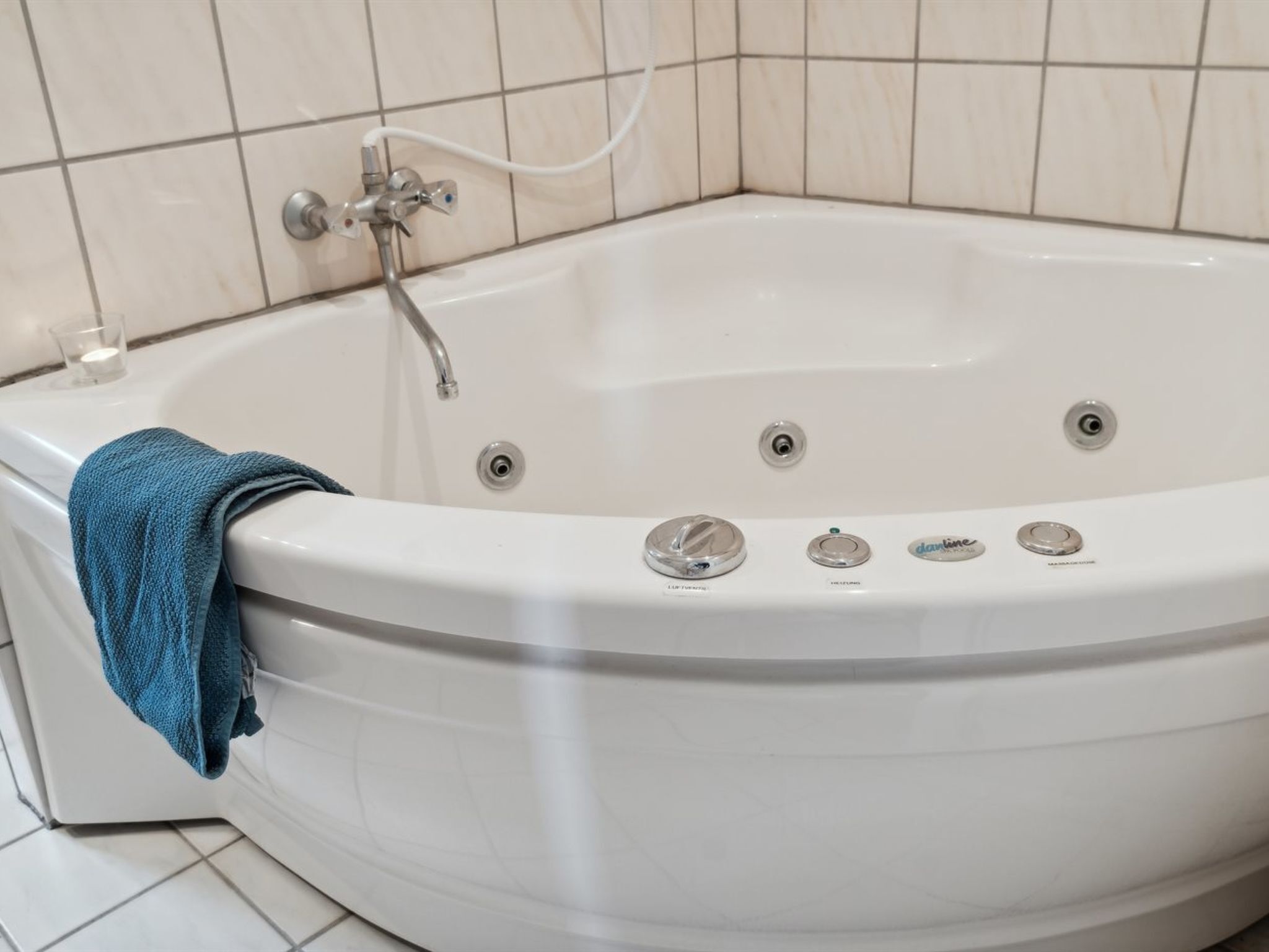 A corner bathtub with a towel, a handheld showerhead, and control knobs.