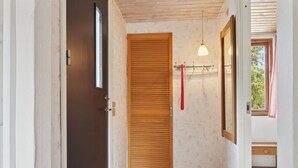Un couloir avec une porte en bois, une petite fenêtre avec un rideau et un luminaire.