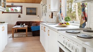 Une cuisine compacte dotée d’un îlot central, d’un coin repas avec une table en bois et d’un espace salon confortable.