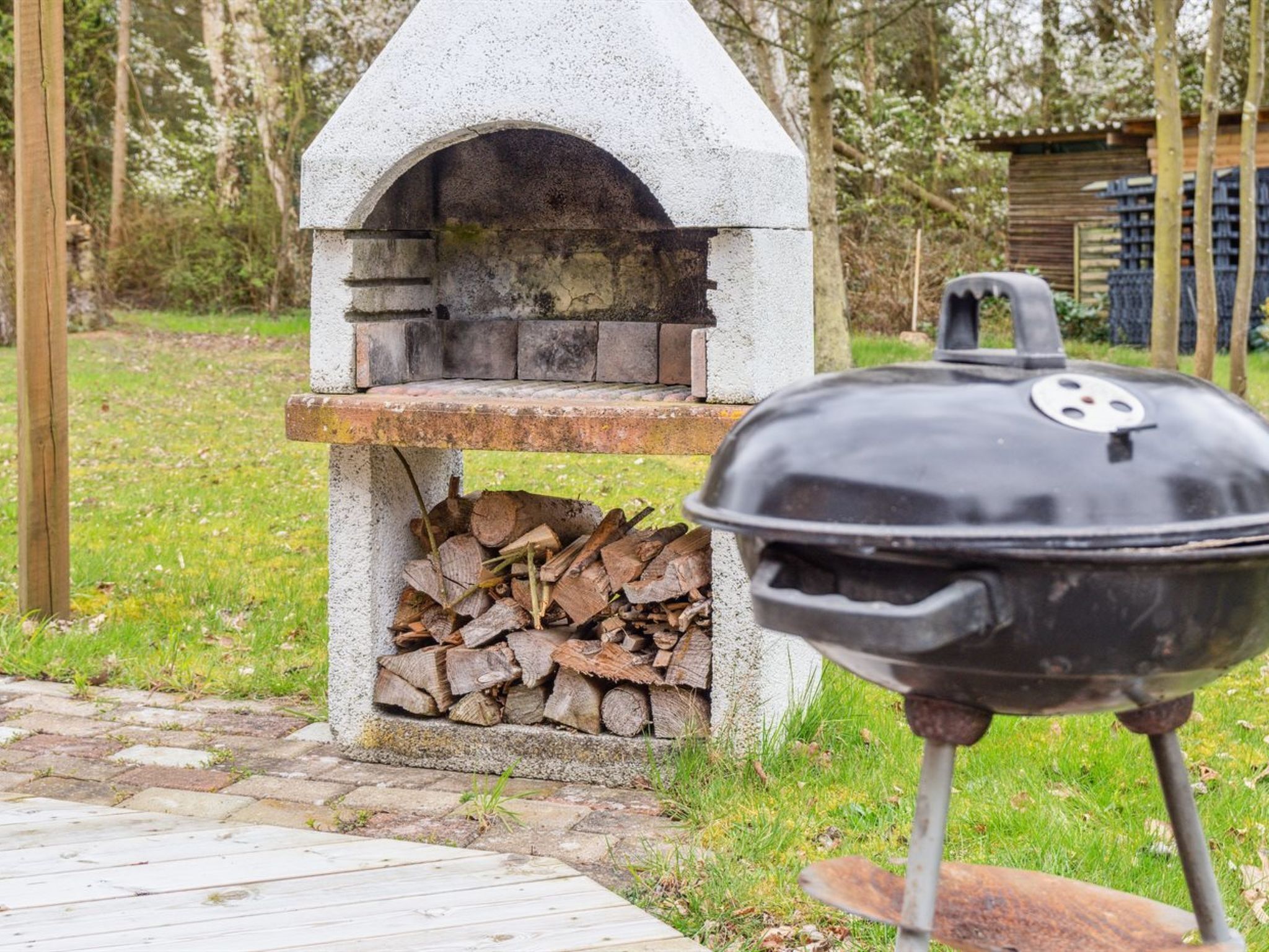 Een barbecue van natuursteen met een schoorsteen, een stapel houtblokken en een metalen grill.