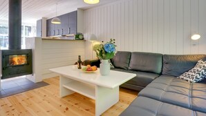A modern living room with a fireplace, a sofa, a coffee table with fruits and flowers, and a kitchen area with cabinets and a radio. - "Bergit" - 55m from the sea by Interhome (Væggerløse)