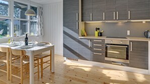 A modern kitchen with wooden cabinets, a dining table with chairs, and a large window providing natural light. - "Bergit" - 55m from the sea by Interhome (Væggerløse)