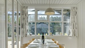 A dining room with a white table set for four, large windows with curtains, and a hanging light fixture. - "Bergit" - 55m from the sea by Interhome (Væggerløse)