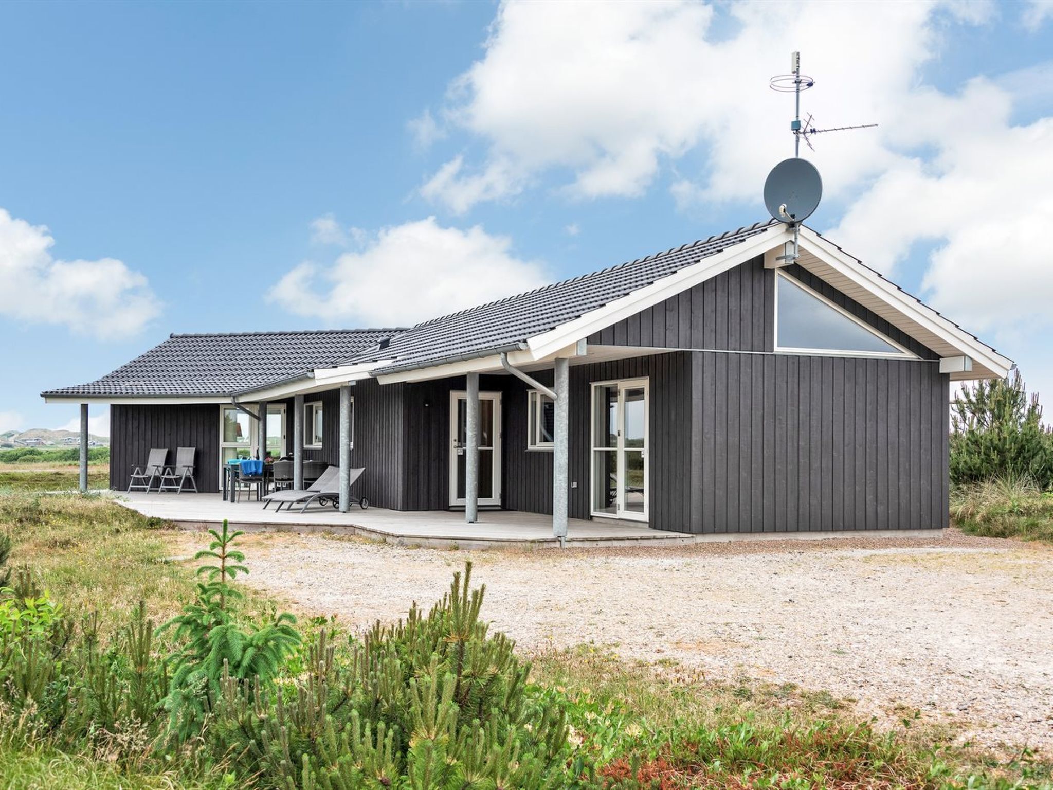 Een modern herenhuis met twee verdiepingen, een overdekte patio, een schotelantenne en een grindpad.