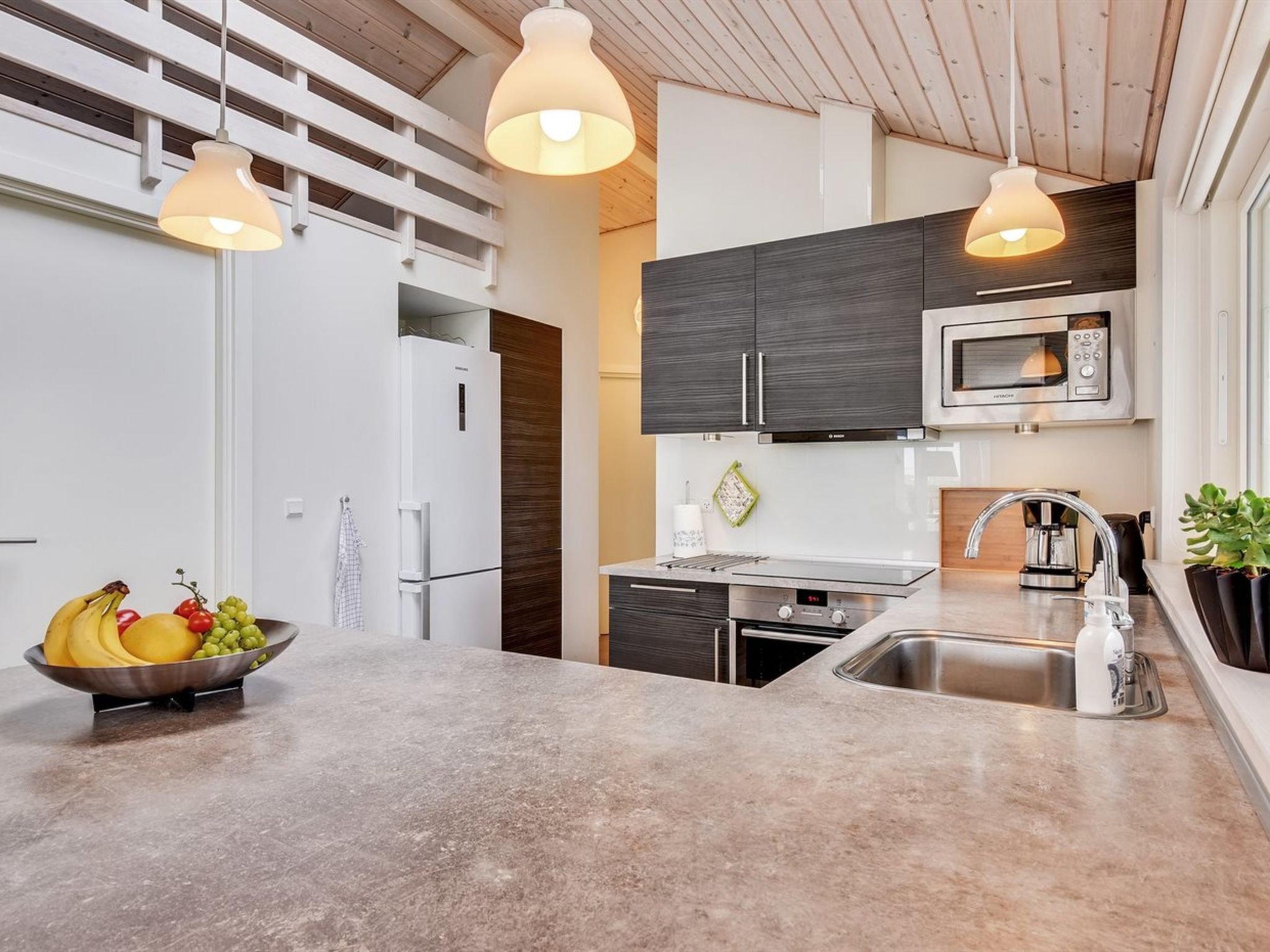 A modern kitchen with a built-in microwave, stainless steel sink, and a fruit bowl on the counter.
