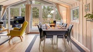 A dining area with a table set for four, a yellow chair, and a television in the background. - "Abiorn" - 2.5km from the sea by Interhome (Blåvand)