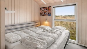 A bedroom with a bed, a wall-mounted shelf, a bedside table with a lamp, and a large window with a view of the outdoors. - "Abiorn" - 2.5km from the sea by Interhome (Blåvand)