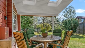 Eine überdachte Terrasse mit einem runden Tisch, vier Stühlen, einem Blumentopf und Blick auf einen Garten und Bäume.