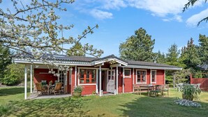 Ein rotes Holzhaus mit überdachter Veranda, Essbereich und kleinem Garten.