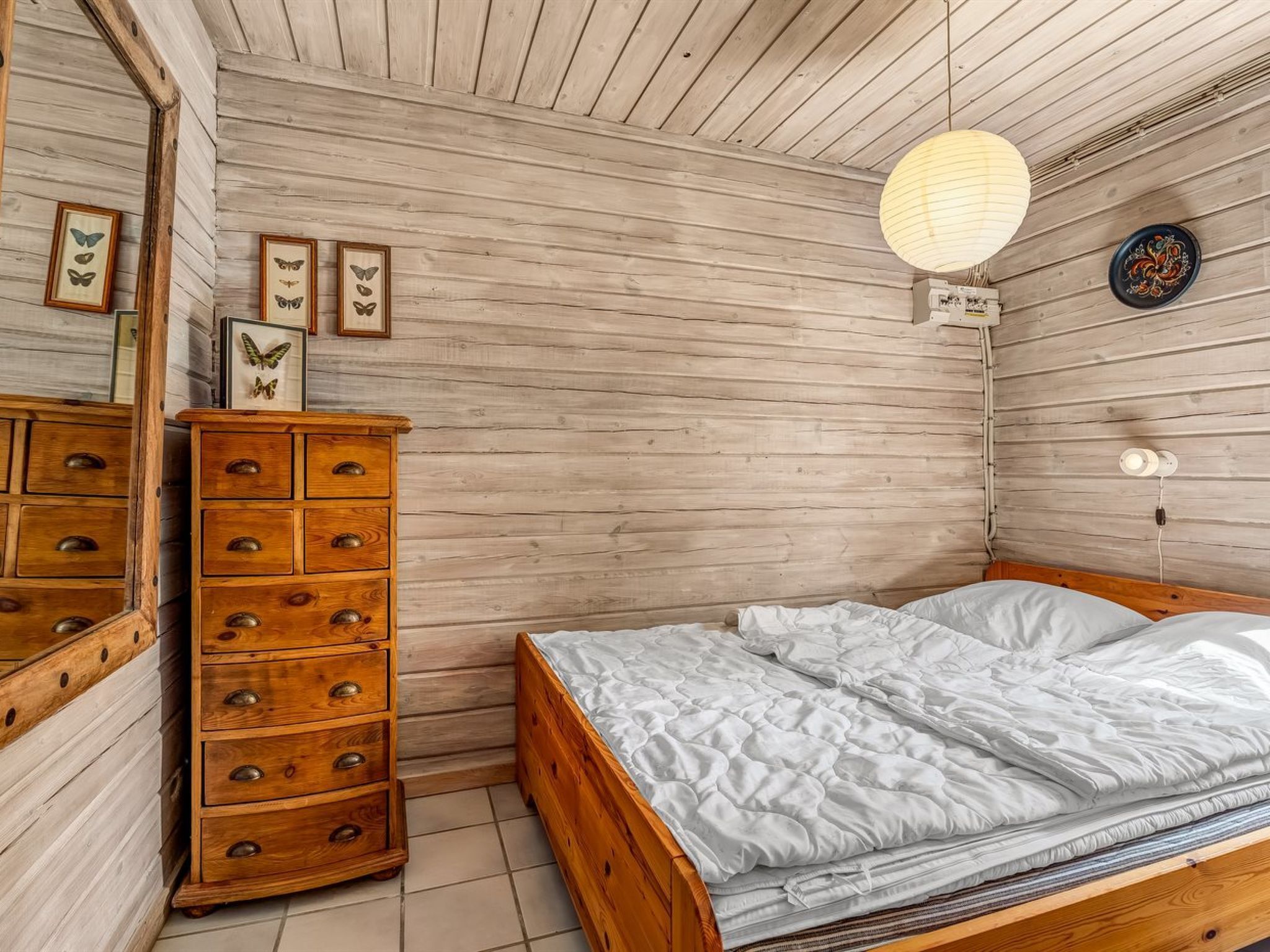A bedroom with a wooden bed, a dresser, a mirror, and butterfly wall art.