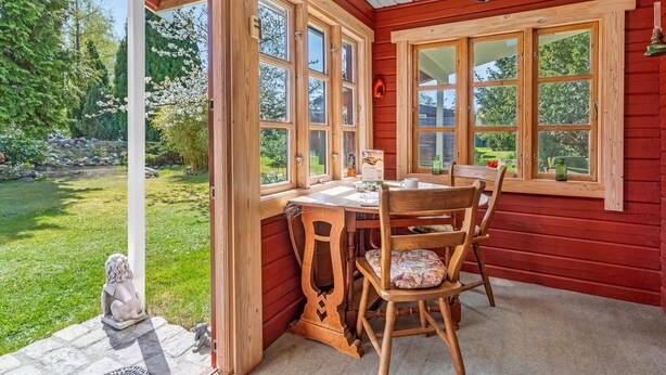 Ein Zimmer aus Holz mit Tisch und Stühlen, großen Fenstern und Blick auf einen Garten.