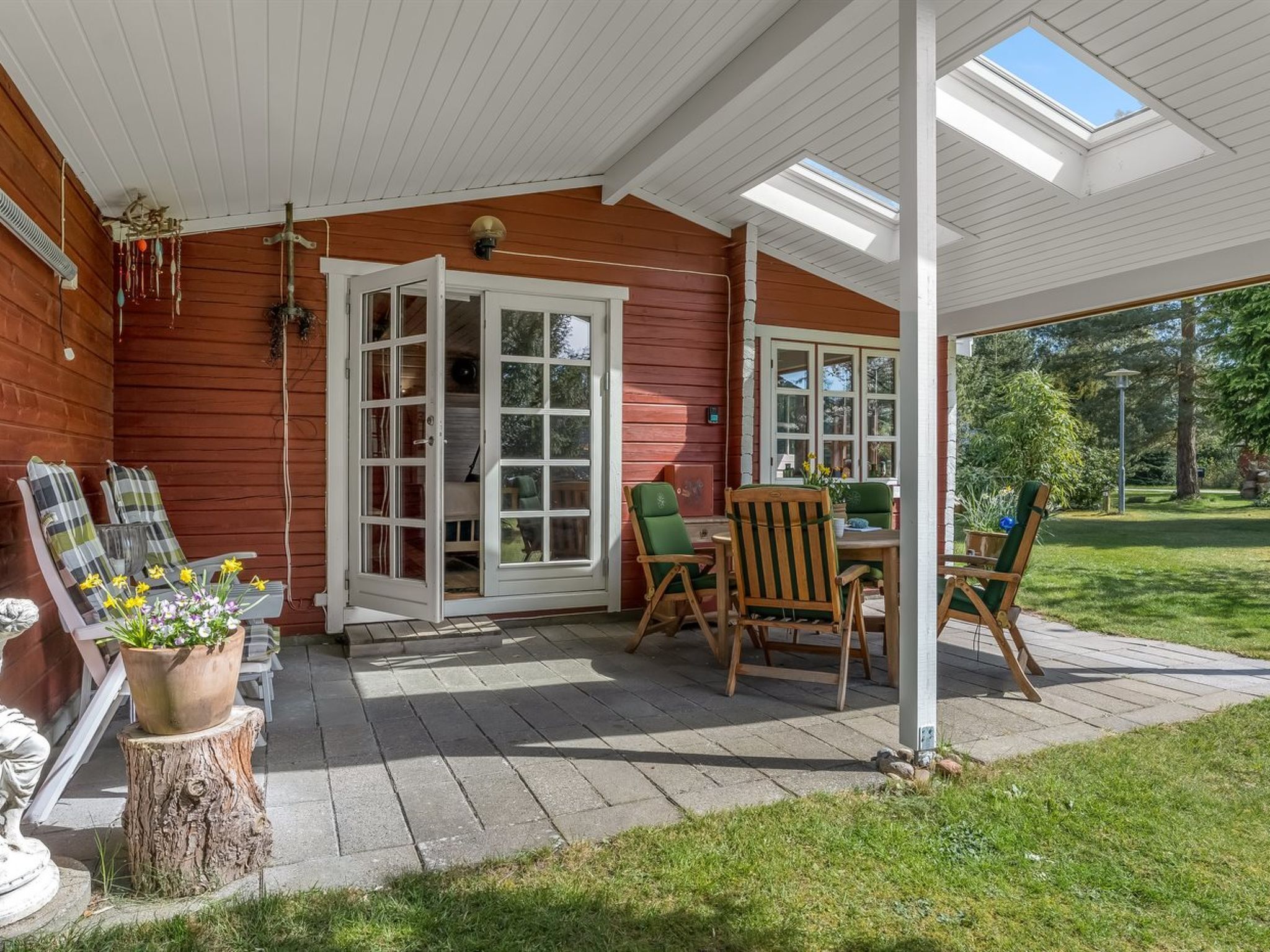 A covered patio with wooden chairs and a table, a wooden deck, and a view of the garden.
