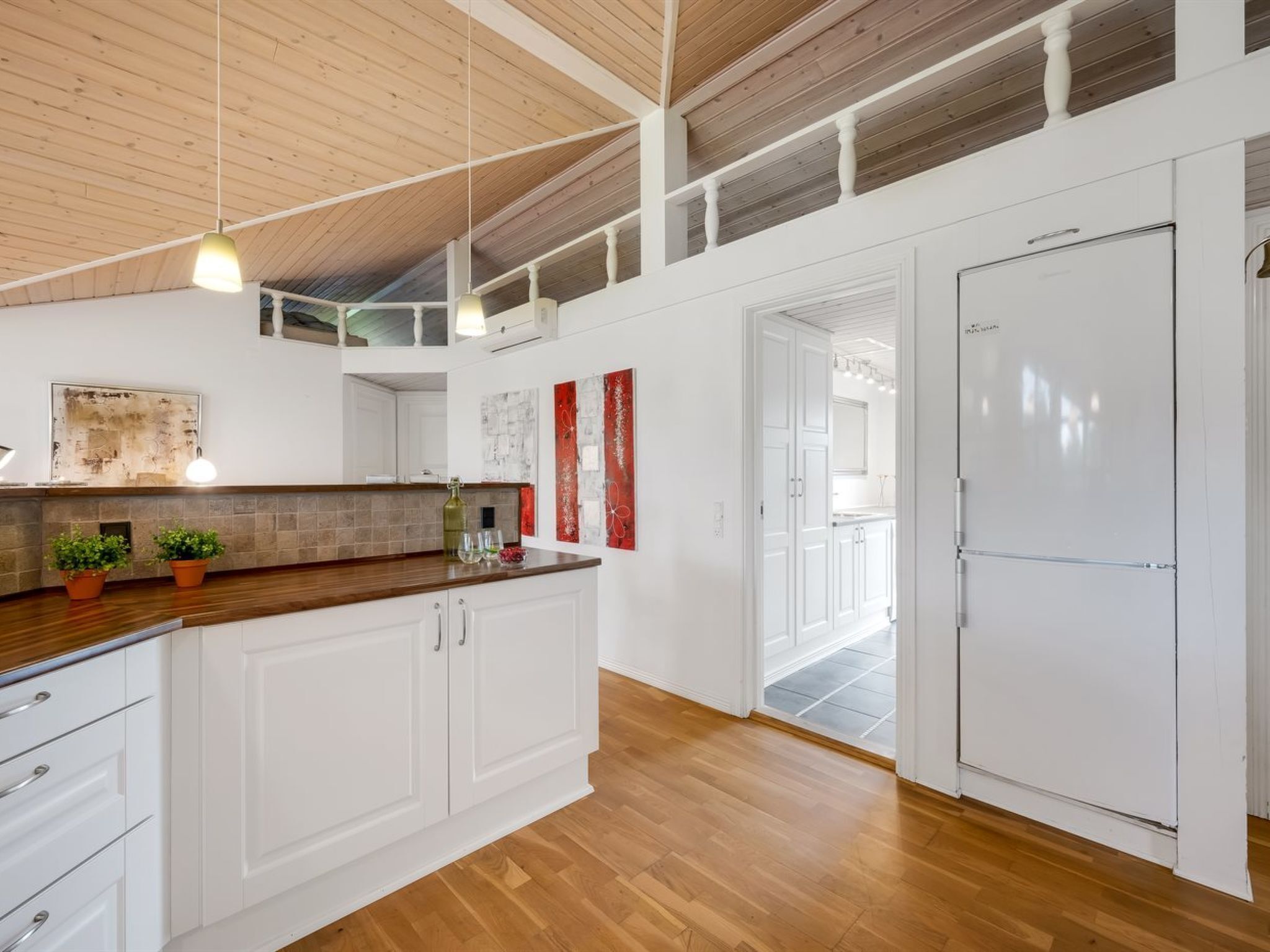 A modern kitchen with wooden flooring, white cabinetry, and a large island.