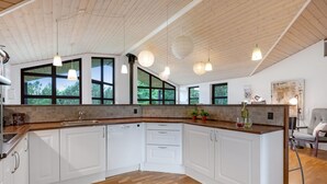 A modern kitchen with white cabinets, a wooden countertop, and large windows.