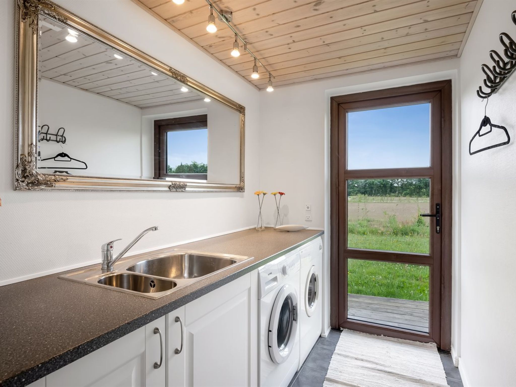 Une buanderie moderne équipée d’un évier, d’un lave-linge et d’un grand miroir.
