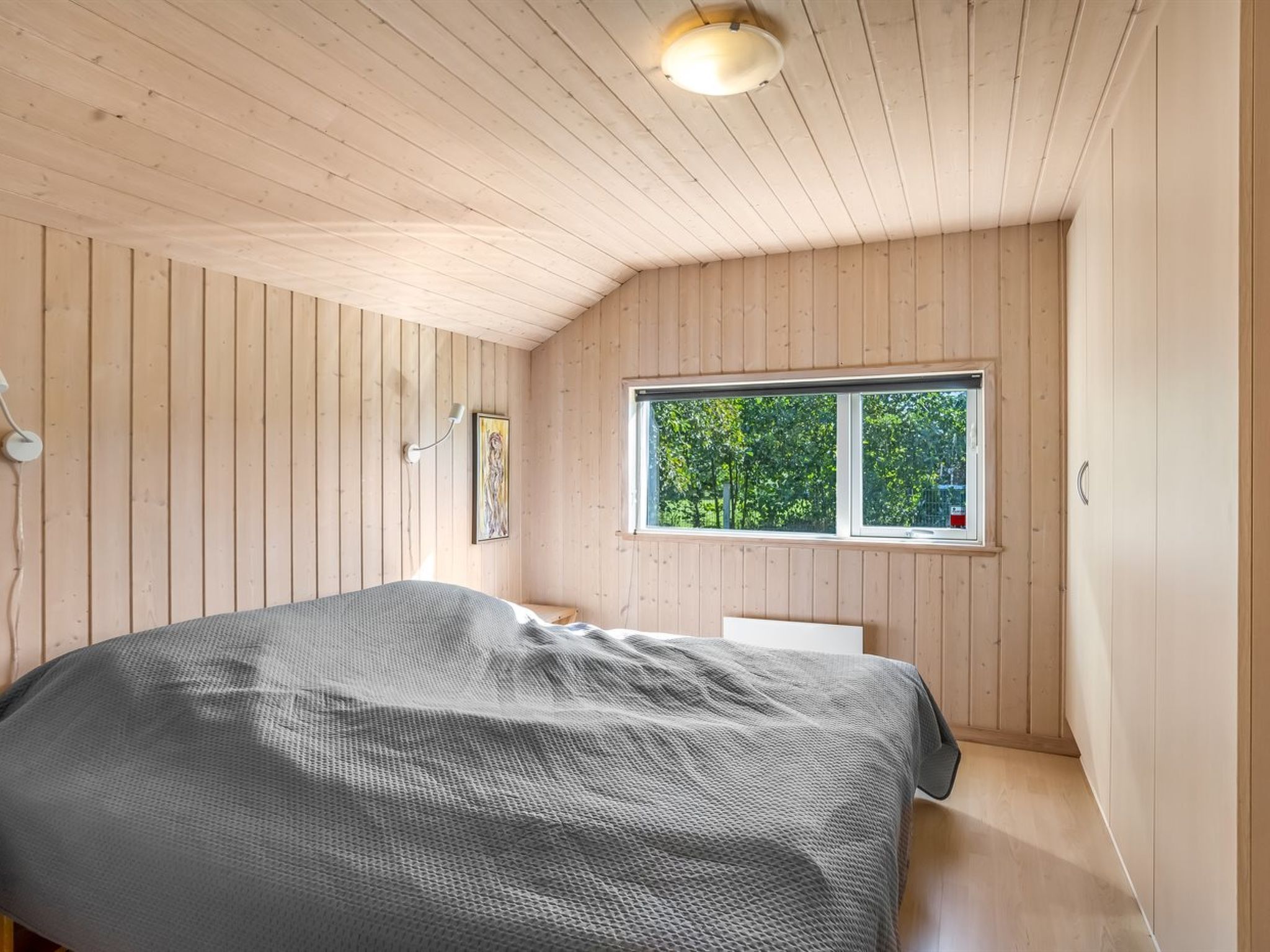 Een slaapkamer met een bed, een raam en houten wanden.