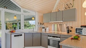 A modern kitchen with grey cabinets, a dishwasher, an oven, and a built-in microwave. There is a window providing natural light and a view of greenery outside. - "Dagny" - 300m from the sea by Interhome (Fanø)