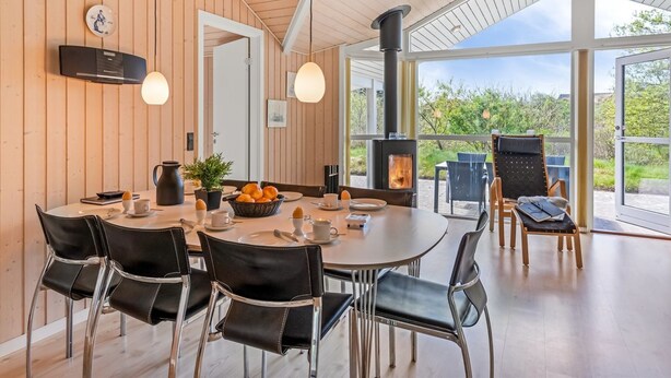 A modern dining area with a round table, black leather chairs, and a large window offering a view of greenery. - "Dagny" - 300m from the sea by Interhome (Fanø)