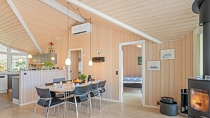 A modern kitchen with wooden walls and a central island, a dining area with chairs and a table, and a visible fireplace. - "Dagny" - 300m from the sea by Interhome (Fanø)
