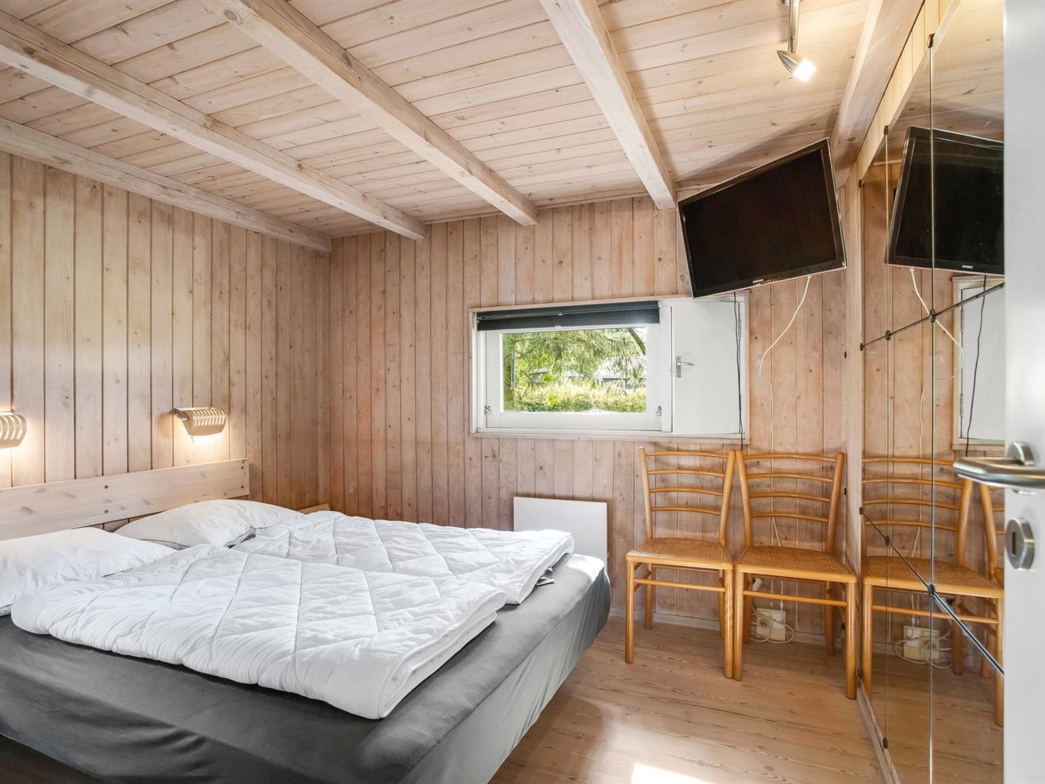 Une chambre dans une cabane en bois, avec un lit, une fenêtre, un téléviseur et une chaise.