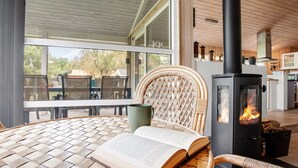 A cozy reading nook with a wicker chair, a table, and a book. A wood-burning stove is visible in the background. - "Fatlinda" - 1km from the sea by Interhome (Væggerløse)