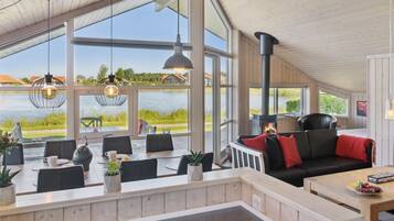 A spacious room with a large window overlooking a lake, a fireplace, and several seating areas.