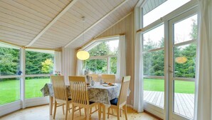 A dining area with a table set for four, surrounded by wooden chairs, large windows, and a view of a green landscape. - "Lyra" - 800m from the sea by Interhome (Væggerløse)