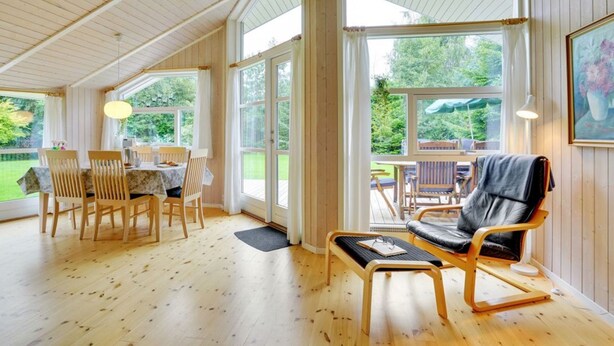 A spacious room with wooden flooring, a dining area with a table and chairs, a seating area with a chair and a bench, and large windows offering a view of the outdoors. - "Lyra" - 800m from the sea by Interhome (Væggerløse)