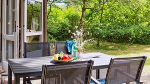 Ein Essbereich im Freien mit Tisch und Stühlen, einer Blumenvase und Blick auf einen üppigen Garten.