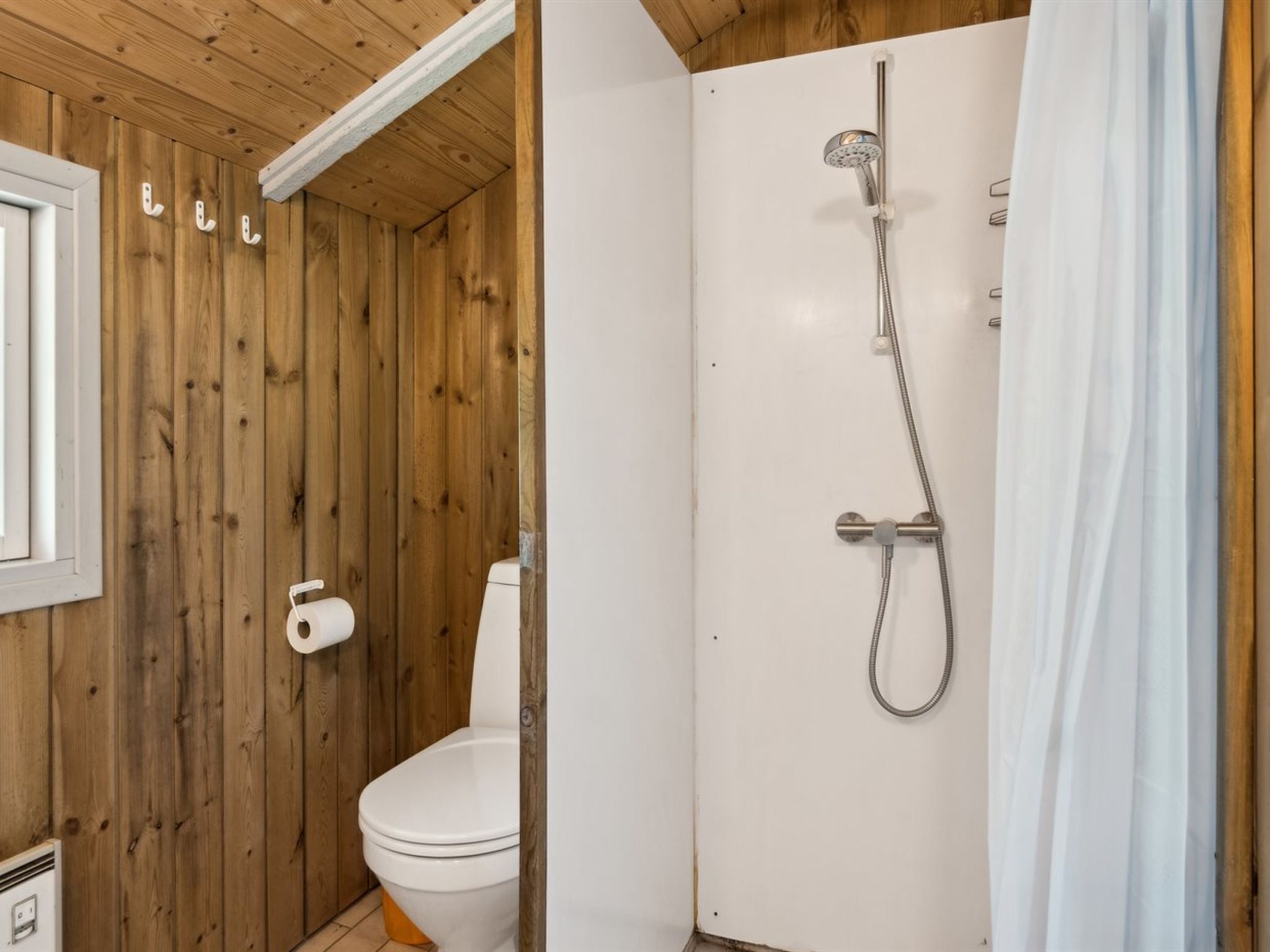 A wooden-paneled bathroom with a toilet, a shower, and a white door.