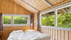 Ein Schlafzimmer einer Holzhütte mit einem Bett, zwei Fenstern und Blick auf Grün.