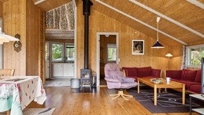 Ein gemütliches Blockhauss-Interieur mit Holzwänden, Kamin, Essbereich und Wohnzimmer mit Couch und Tisch.