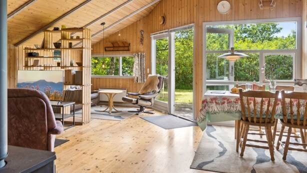 Ein gemütliches Blockhauskaminzimmer mit Holzwänden und geneigter Decke, das eine Sitzecke mit einer Couch, einen Esstisch mit Stühlen und einen Kamin bietet.