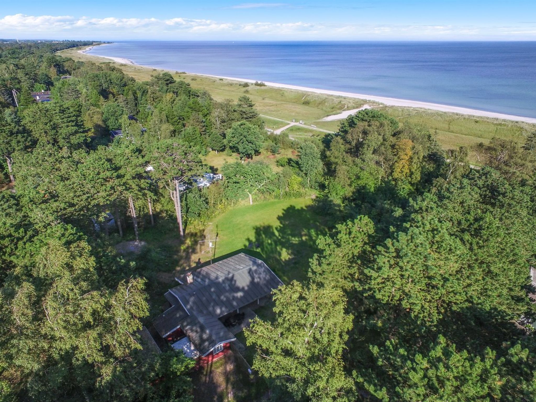 Eine Luftaufnahme eines Küstengrundstücks mit Strand, dichtem Wald und einem Haus mit rotem Dach.