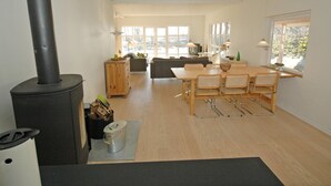 A spacious living area with a large window, a dining table with chairs, a sofa, and a black wood-burning stove. - "Borica" - 100m from the sea by Interhome (Væggerløse)